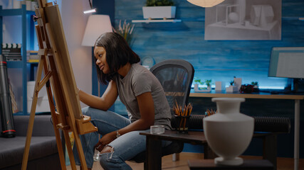 Artist of african american ethnicity drawing white vase design on canvas with pencil sitting in art studio at home. Black young woman getting authentic inspiration for modern masterpiece