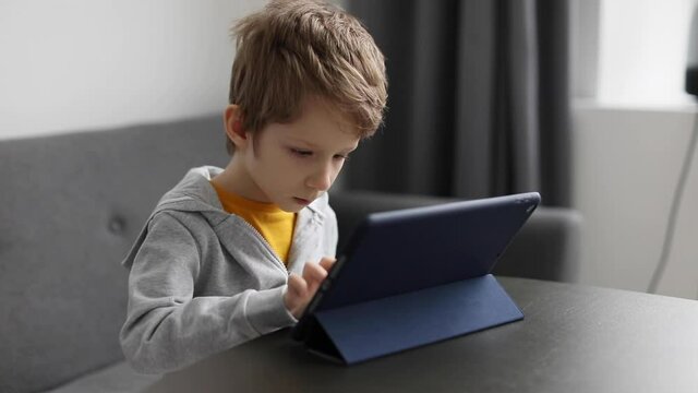 Cute little boy using pad. Child plays digital tablet at home. Free time, technology and internet for kids