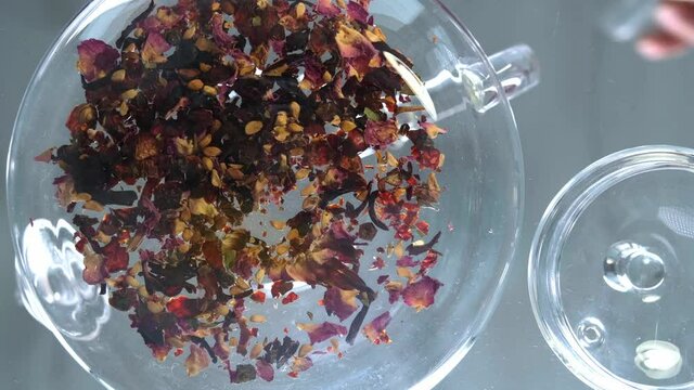 The process of making red tea. Hibiscus tea with rosehip seeds. Petals of rosehip flowers. Bottom view. Through the transparent surface of the glass kettle, the brewing process is clearly visible.