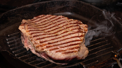 Close-up meat of beef steak grilled in cast-iron ribbed fry pan on gas stove. Delicious juicy meat steak cooking on grill.