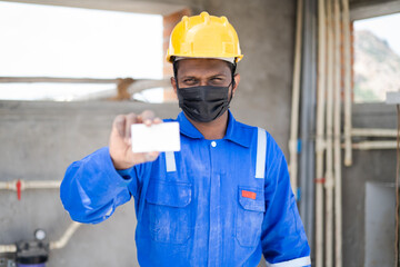 Plumber with medical face mask and safty precautions showing empty card by looking at camera -...