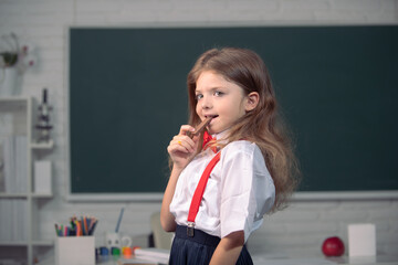 Cute child eating chocolate sweets at school. Kid is learning in class on background of blackboard.
