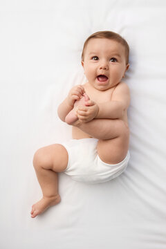 Happy baby lying on white bed holding foot
