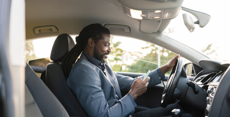 afro american man in car interior while looking at his mobile phone