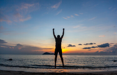 Silhouette Young man with arms raised up on the tropical beach at sunset