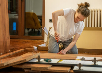 Young smiling woman assembling furniture at home using a screwdriver while sitting on the floor in a new house