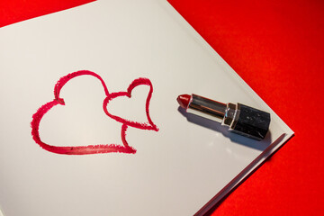 Two hearts are drawn with red lipstick in a notebook on a red background. Love message for Valentine's Day. High quality photo