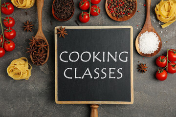 Small chalkboard with inscription Cooking Classes and different fresh products on grey table, flat...