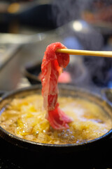 Hand using chopsticks to pick up raw sliced beef for eating Shabu Shabu or Japanese sukiyaki