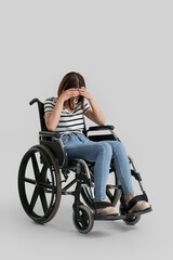Fototapeta na wymiar Depressed young woman in wheelchair on light background