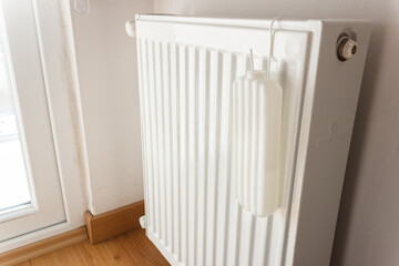 Heating radiator at home. Water pot is hanging on radiator for moistening. 