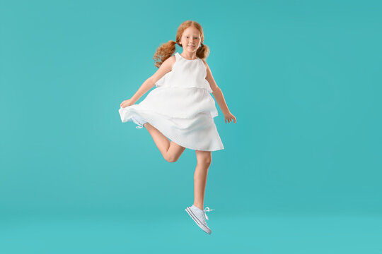 Little redhead girl in white dress jumping on blue background