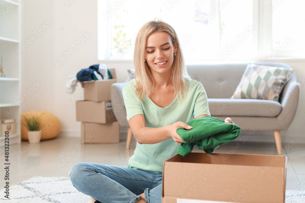 Wall mural young woman putting clothes in box for donation at home - Wall murals