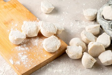 Uncooked dumplings sprinkled with flour on a white table.