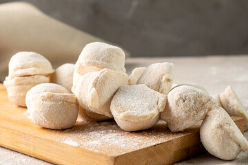 Uncooked dumplings on a white table sprinkled with flour close-up.
