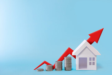 Stack of coins arranged in ascending order with house model and red arrow graph growing value in blue background for business investment real estate concept.