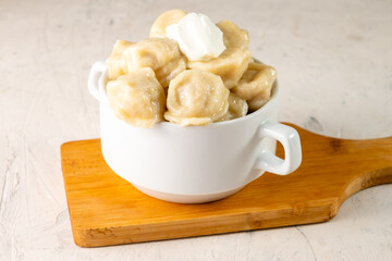 Cooked dumplings with sour cream in a cup on a white table.