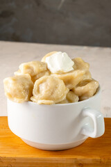 Homemade meat dumplings served in a white bowl with sour cream, close-up. Vertical photo.
