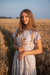 Portrait of beautiful young girl with a bouquet of spikes. Girl in white dress in the field of rye