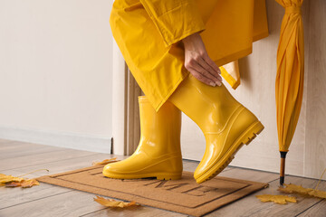 Woman wearing yellow gumboots on floor mat near light door