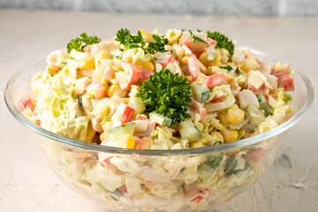 Crab salad with vegetables and crab sticks in a transparent bowl, close-up.