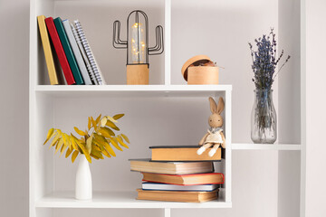 Shelf unit with different books, vases and decor near white wall