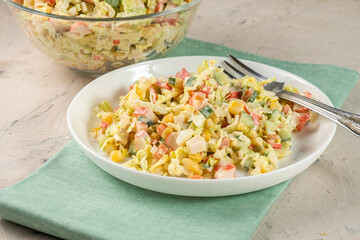 Classic crab salad with surimi sticks and vegetables in a white plate on a blue rag.