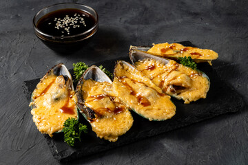 Baked mussels with cheese in shell halves on a dark table.