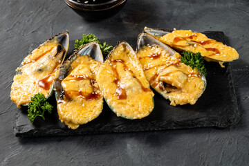 Starter of baked mussels with cheese, unagi sauce and sesame seeds. Five pieces. Dark table.