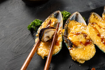 Mussel snack. Baked mussels with cheese. Mussels are eaten with chopsticks. Close-up.