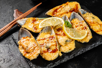 Mussels in shell halves baked with cheese sauce and served with a slice of lemon on a stone tray.
