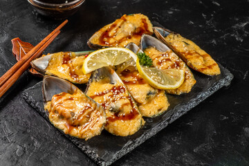 Baked mussels under cheese on a dark table.