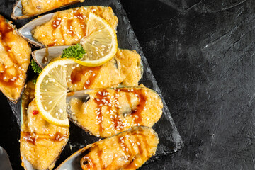 Baked mussels with cheese and teriyaki sauce on a dark table, top view.