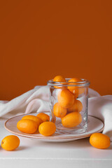 Jar with tasty kumquat fruits on light wooden table
