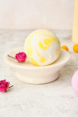 Bowl with bath bomb and dried rose flowers on light background, closeup