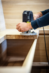 carpenter or craftsman works with a router on a wooden panel