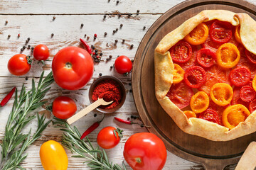 Board with tasty tomato galette on light wooden background