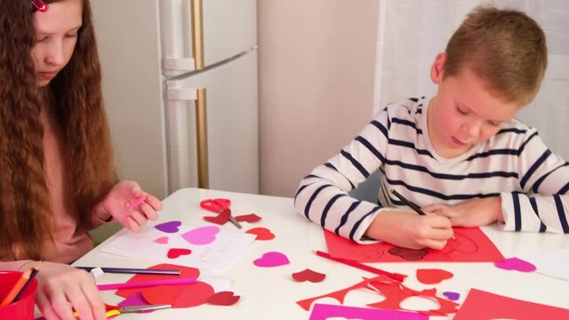 Kids, children, doing Valentine's Day arts and crafts with hearts, pencils, paper. Gift, surprize for mom. Children makes Handmade decorations for holiday. Prepare for Valentine Day. Painting, DIY.