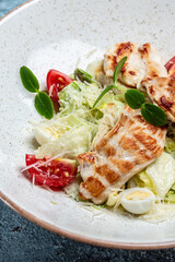 Caesar salad with chicken breast. Female hand sprinkles Parmesan Cheese in a freeze motion, dark wooden background, cooking concept, vertical image. copy space