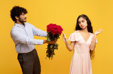 Unwanted confession. Displeased indian lady rejecting her admirer with roses on Valentine's Day, yellow background