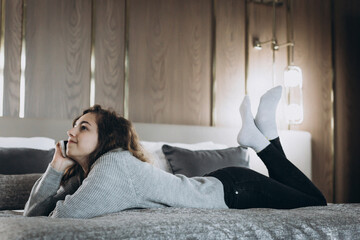 Happy smiling teenager girl talking by phone lying on the bed