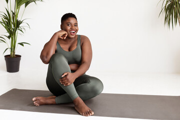 Excited overweight black woman sitting on yoga mat