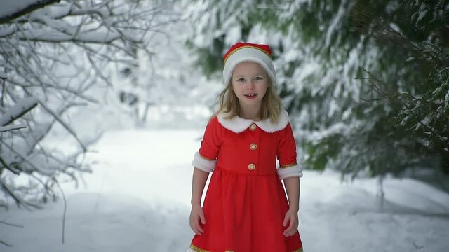 Happy christmas girl smille in santa costume in snow. Winter forest with snowdrifts and snacks. child laughs at new year and walks outside. red suit hat. Dance have fun. Portrait laughing childhood.