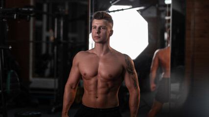 Obraz na płótnie Canvas Handsome young athlete man bodybuilder with naked muscular torso trains in the gym on a dark background