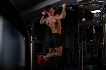 Naklejka na ściany i meble strong bodybuilder man in good physical shape and a naked muscular body pulls up in the sports gym against a dark background
