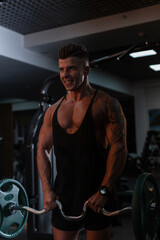Fototapeta na wymiar Strong athletic bodybuilder man in a black t-shirt pumps muscles in the gym on a dark background