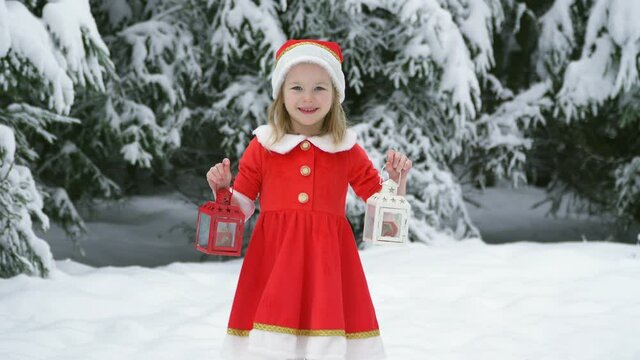 Happy christmas girl candlestick dance smille in santa costume in snow. Winter forest with snowdrifts and snacks. child dance walks outside. red suit hat. have fun. Portrait laughing childhood.