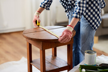 repair, diy and home improvement concept - close up of woman with ruler measuring old round wooden...