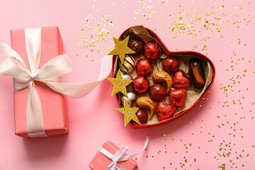 Heart shaped box with tasty chocolate candies and gifts on pink background