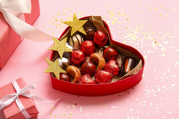 Heart shaped box with tasty chocolate candies and gifts on pink background